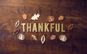 Cut out letters that spell Thankful laid out on a table surrounded by cut out leaves and pumpkins.